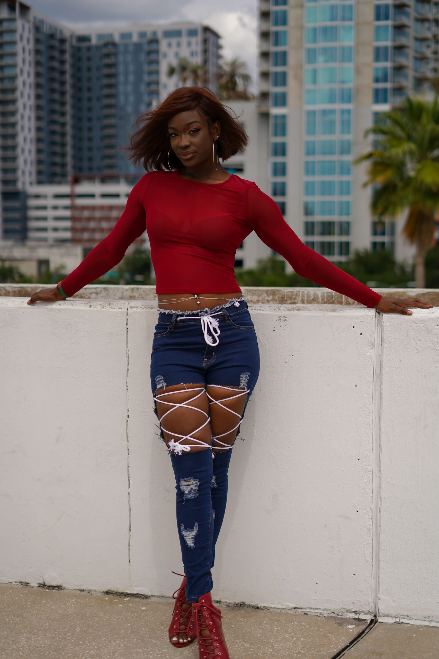 Woman wearing a red blouse and distressed jeans against an urban backdrop
