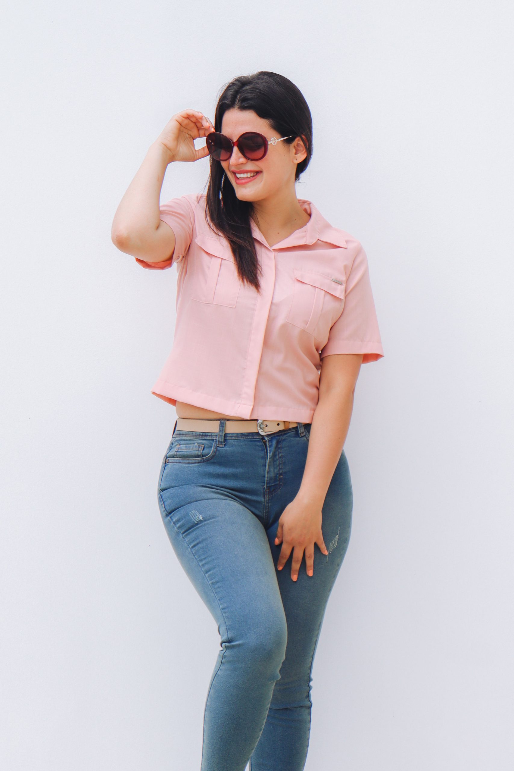 Woman wearing a pink short sleeve blouse with jeans and holding sunglasses