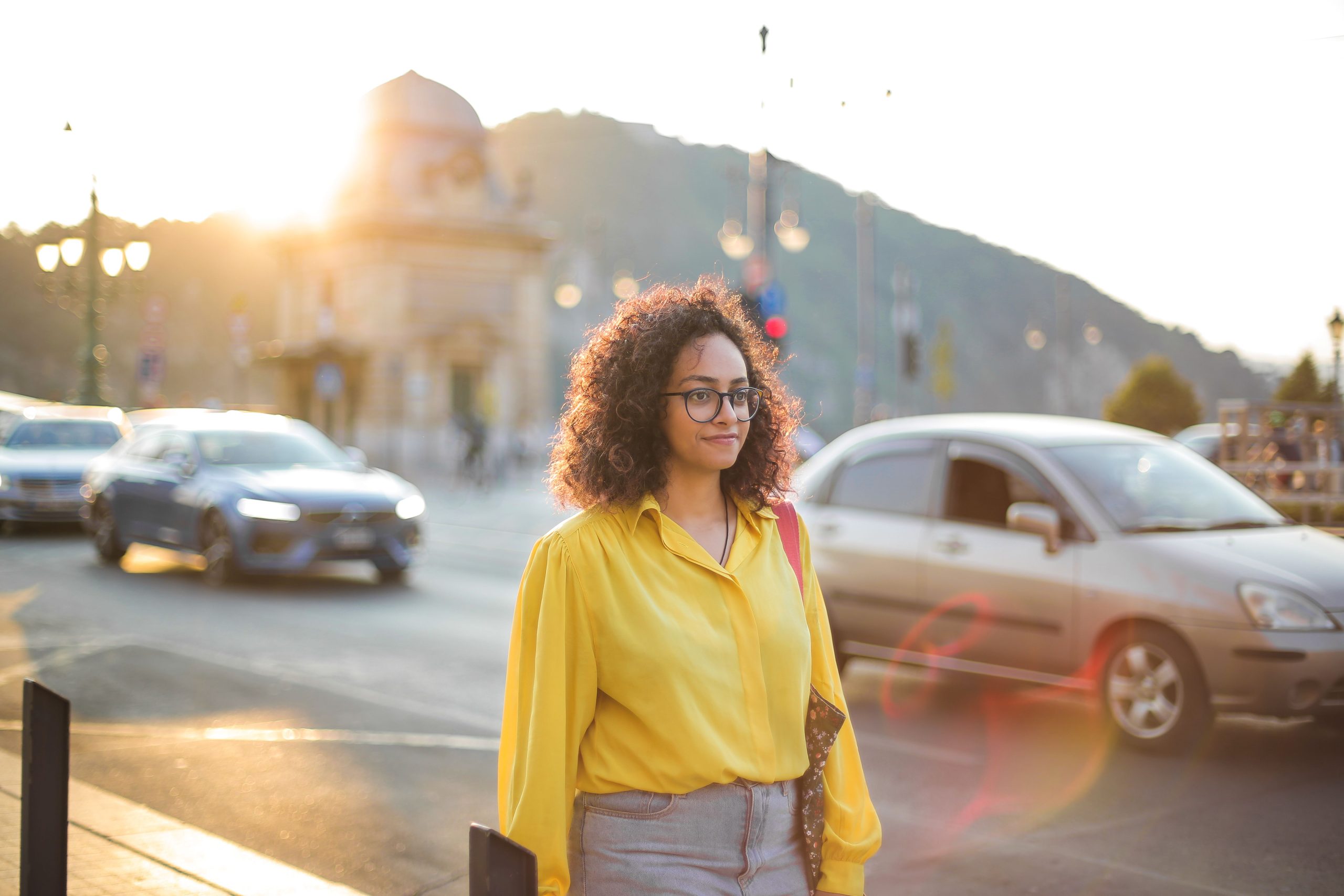 Woman wearing a yellow button up shirt and blue jeans while walking on a city street