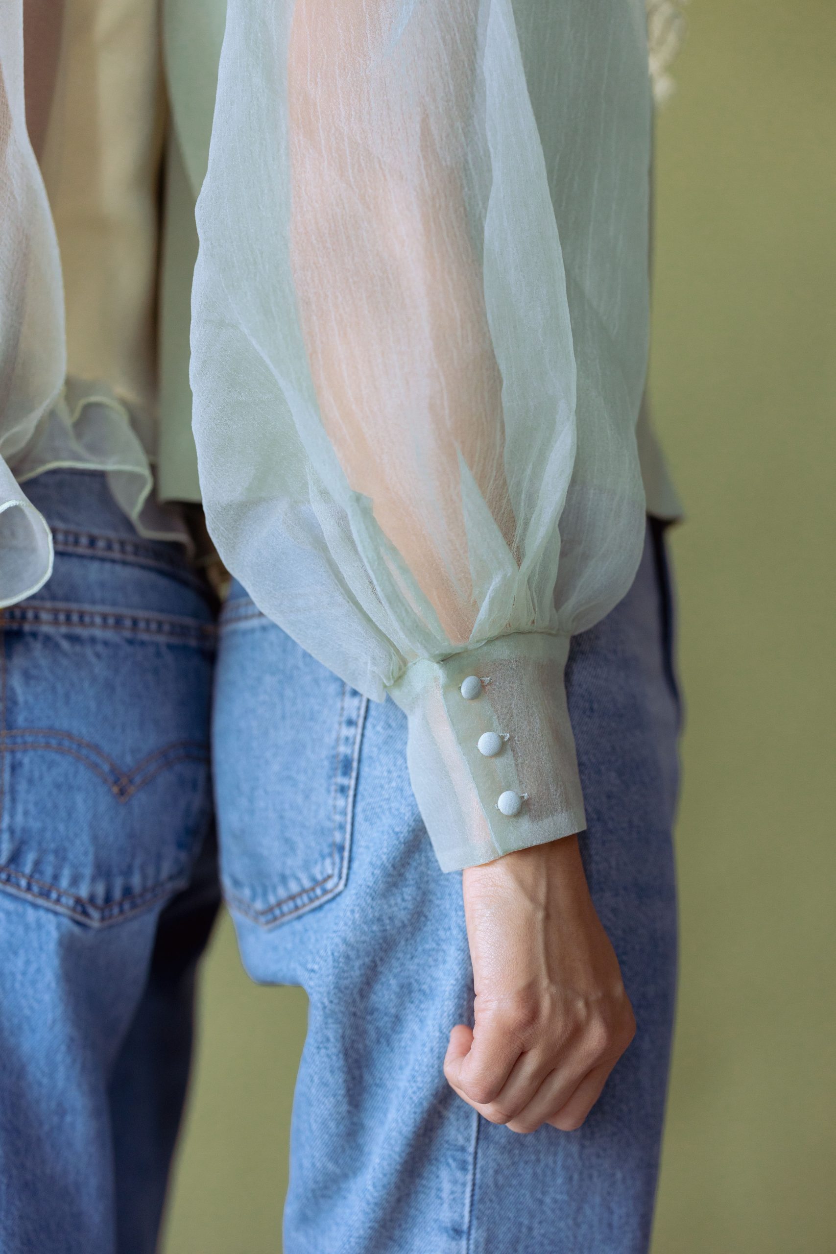 Close up of a soft green chiffon blouse worn with blue denim jeans