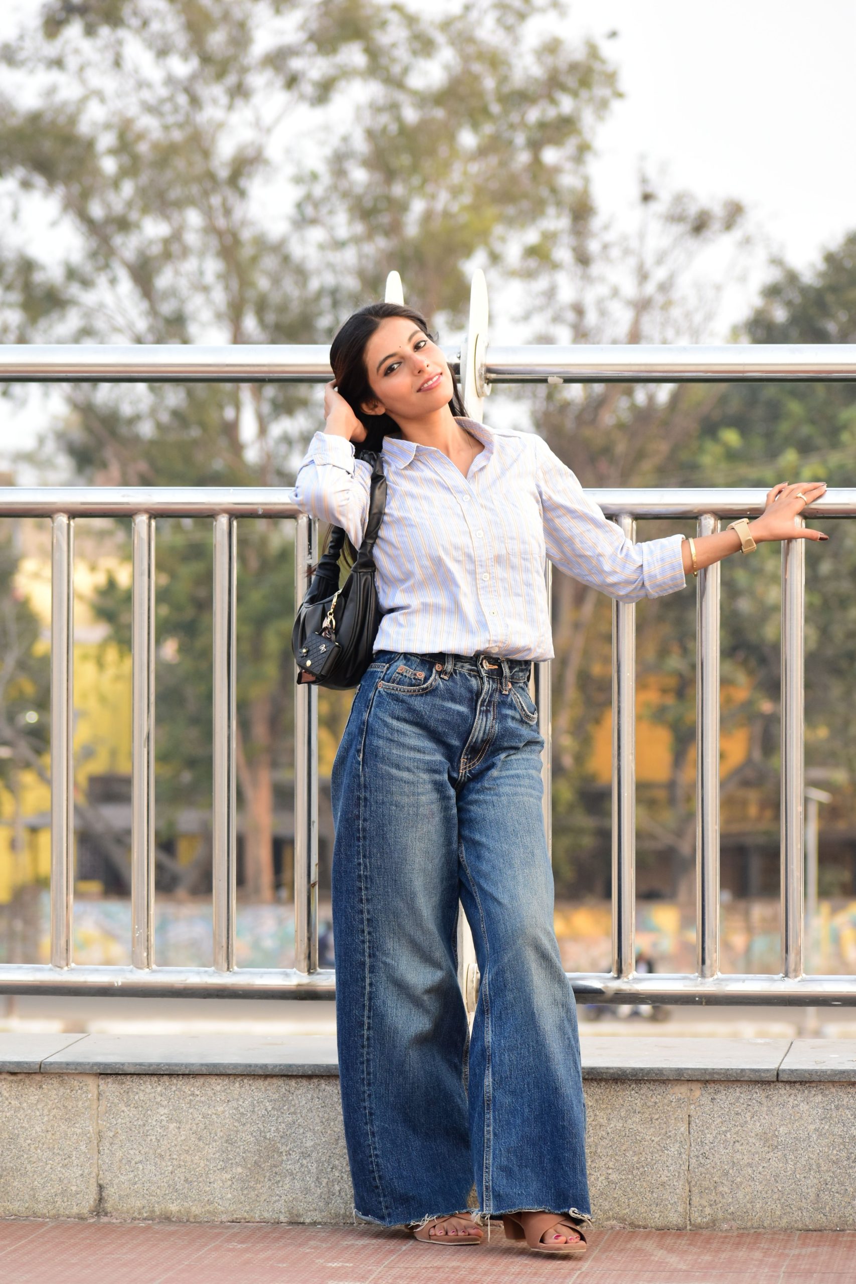 Woman wearing a white shirt and wide-leg jeans outdoors beside railings